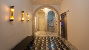 A hallway with a checkered floor, an elevator, and a staircase leading to another floor.