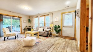 A cozy living room with a sofa, coffee table, and chair, a wooden floor, and large windows with curtains. - Cozy cabin on 5 acres of wooded land! (Wausaukee)