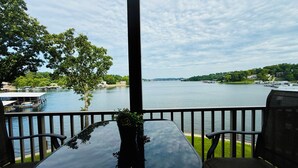 A terrace with a table and chairs overlooking a river, with boats and buildings in the background. - Luxe Lakefront, King & Queen Bed Suites, Sunset, Pools, Boat Slip, 1,786 sqft! (Osage Beach)