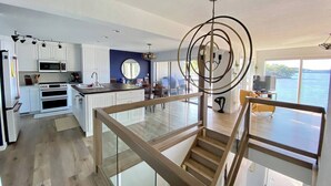A modern kitchen with white cabinets, a central island, and a dining area with a view of the water. - Luxe Lakefront, King & Queen Bed Suites, Sunset, Pools, Boat Slip, 1,786 sqft! (Osage Beach)