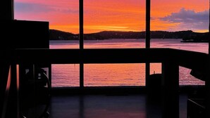 A room with a large window overlooking a body of water during sunset. - Luxe Lakefront, King & Queen Bed Suites, Sunset, Pools, Boat Slip, 1,786 sqft! (Osage Beach)