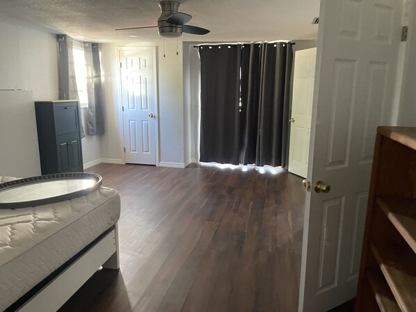 Quarto com ventoinha no teto, porta com cortina, porta branca, piso de madeira e parede branca.