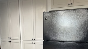 Una cucina con mobili bianchi, un frigorifero nero e un piano di lavoro in legno.