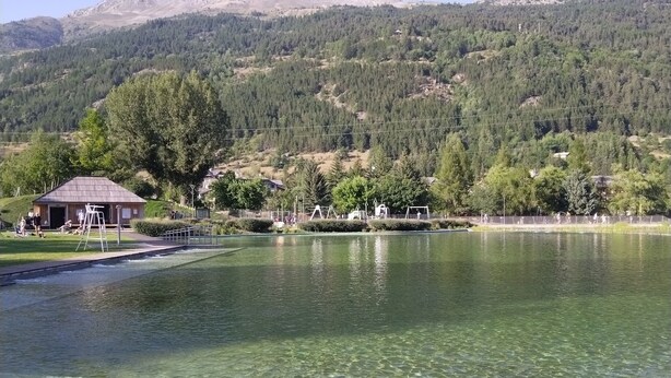 Un lac avec une jetée en bois au premier plan, entouré d’une chaîne de montagnes boisées.