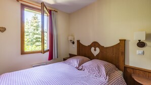Une chambre à coucher avec un lit, deux lampes de chevet, une fenêtre avec des rideaux et un radiateur fixé au mur.