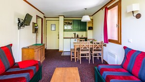 Un espace de vie compact comprenant un coin cuisine, deux canapés, une table à manger et un téléviseur fixé au mur.