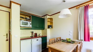 Une cuisine compacte équipée d’un four à micro-ondes, d’un évier et de meubles de rangement verts. On y trouve une table à manger avec des chaises et un plateau de fruits.