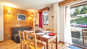 A dining area with wooden furniture, a table set for four, and a view of a parking area outside. - Le Silène - Appt pour 6 (Chamrousse)
