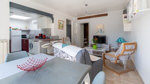 Un espace de vie compact comprenant un coin repas, une petite cuisine, un coin salon avec un téléviseur et un fauteuil relaxant.