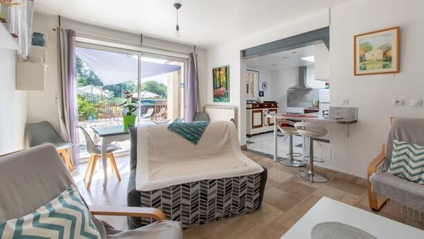 Un salon moderne avec un canapé, des fauteuils, une table à manger et une cuisine en arrière-plan.