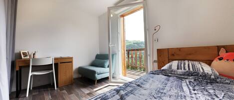 A bedroom with a bed, a desk, a chair, and a balcony with a view.