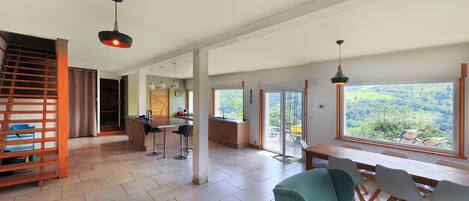 A spacious living area with a large window, a dining table, and a staircase.