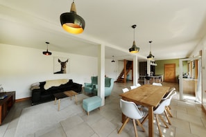 A spacious living area with a wooden dining table, light blue armchairs, and a black sofa. There are pendant lights above the table and a staircase leading to another level. - La Bergerie du Pré de l'Orme - Avec vue montagne (La Bresse)