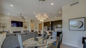 Een moderne woonkamer met een glazen eettafel, grijze banken en een plafondventilator.