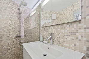 Een moderne badkamer met een ruime wastafel, een douche met handdouche en een spiegel boven de wastafel.