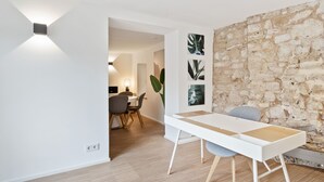A modern dining area with a white table and chairs, a stone wall, and a plant. - Modern Apt Old Town w Panoramic View ID4 (Luxembourg City)