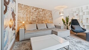 A modern living room with a stone wall, a grey sofa, a white coffee table, a black chair, and a white shelving unit. - Modern Apt Old Town w Panoramic View ID4 (Luxembourg City)