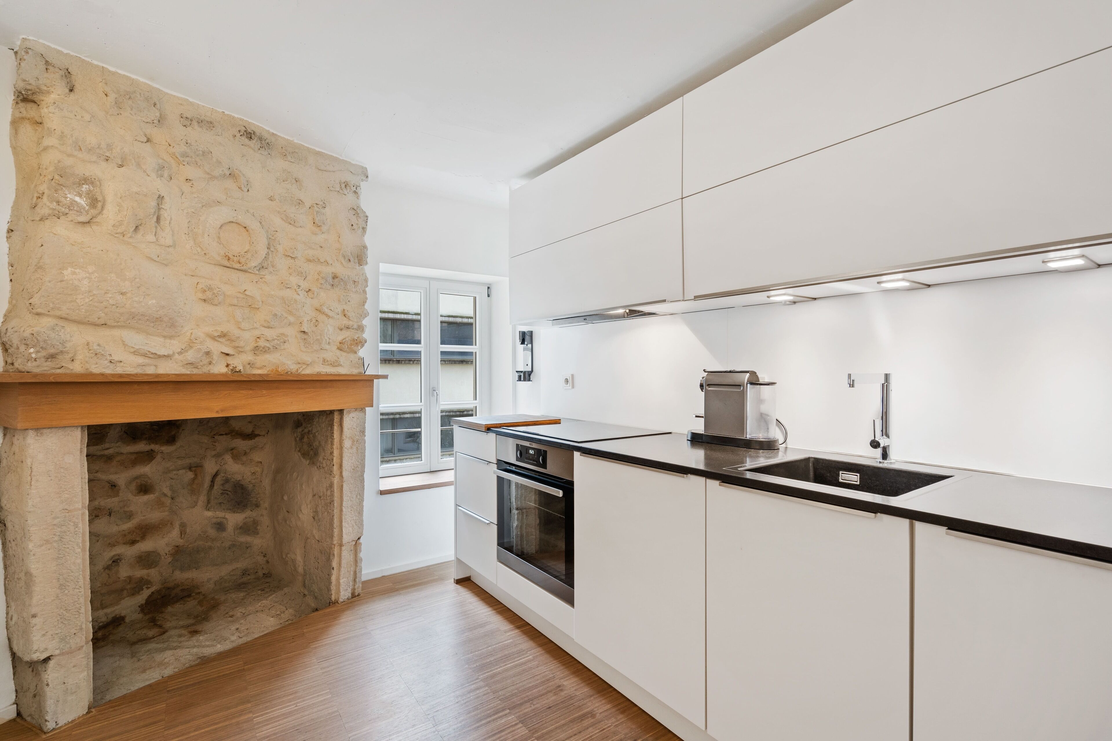 A modern kitchen with white cabinets, a stone fireplace, and a built-in oven.