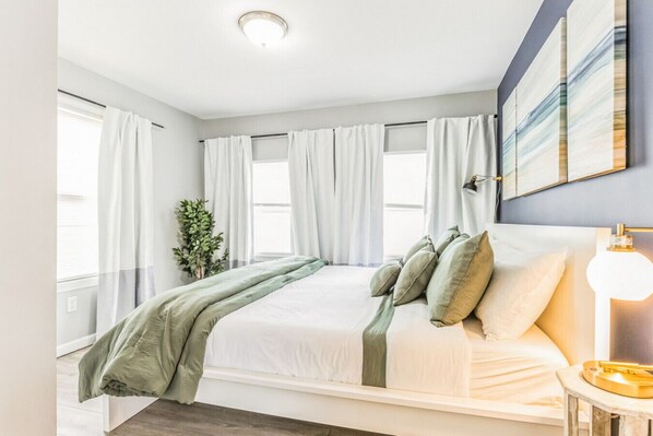 A bedroom with a bed, curtains, a bedside lamp, and a plant.