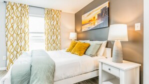 A modern bedroom with a bed, two bedside lamps, a nightstand, and a painting on the wall.