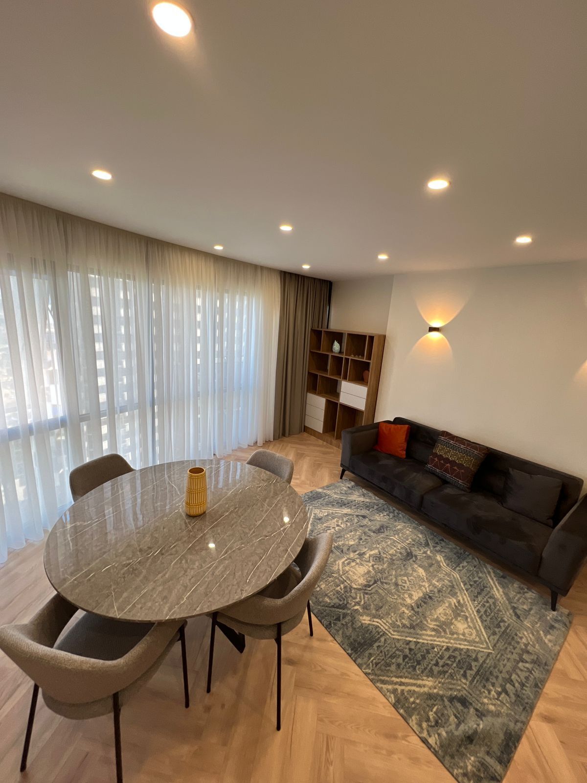 A modern living room with a round dining table, a sofa, and a patterned rug.