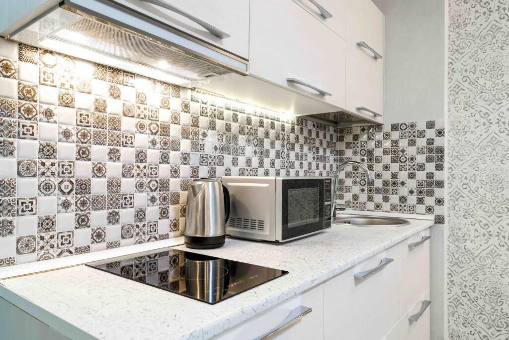 Una cocina moderna con baldosas estampadas, un hervidor de acero inoxidable, un microondas y una placa de inducción integrada.