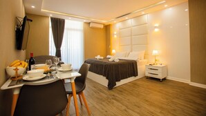 Une chambre d’hôtel comprenant un lit, des tables de chevet, un coin repas avec une table dressée pour deux personnes, et un téléviseur fixé au mur.