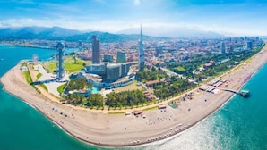Vue aérienne d’une ville côtière, avec un imposant complexe de bâtiments modernes, une plage et une étendue d’eau.