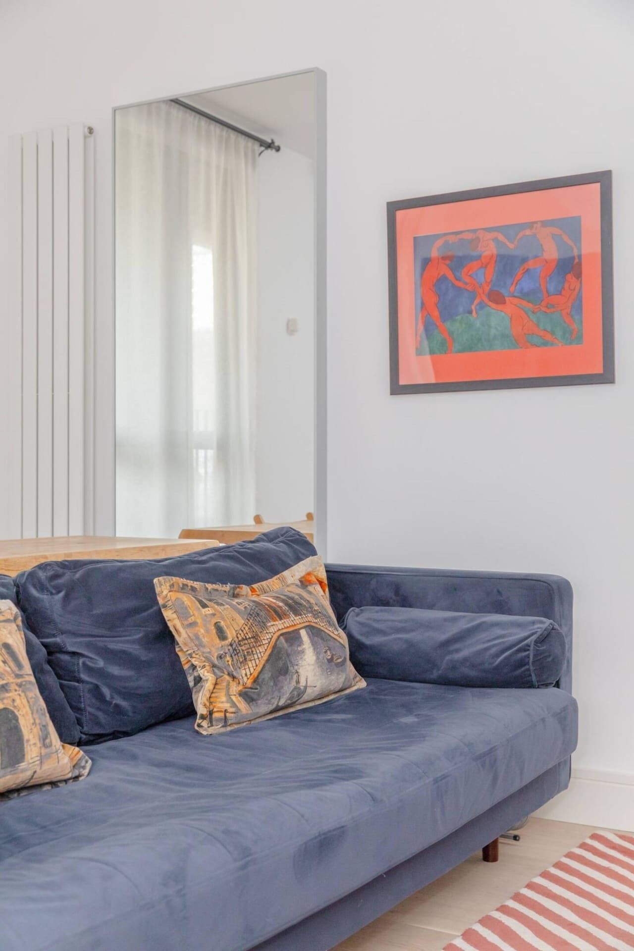 A room with a blue sofa, patterned pillows, a large mirror, and a framed artwork on the wall.