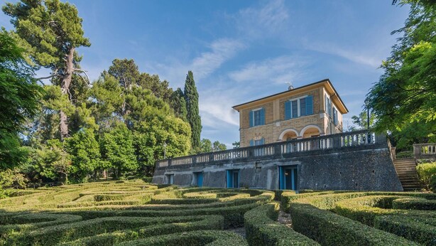 Un bâtiment historique, avec un pont de pierre, des jardins bien entretenus et un ciel d’un bleu éclatant.