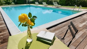 Un espace aménagé au bord de la piscine, avec une table, un vase rempli de fleurs jaunes et un livre.
