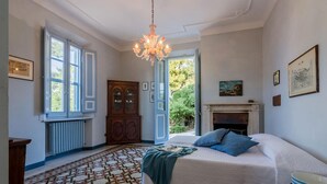 Une chambre à coucher avec un lit, un lustre, une cheminée et une grande fenêtre.