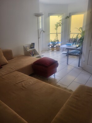 A living room with a sofa, a red ottoman, a small table with a bowl, and a potted plant.