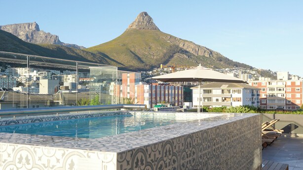 A rooftop pool with a patterned tile design, surrounded by buildings and a mountain in the background. - Six on N 302 (Cape Town)