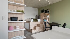 A modern, well-lit room with built-in shelving, a flat-screen TV, a bed with a green blanket, and a dining area with a table and chairs. - Six on N 302 (Cape Town)