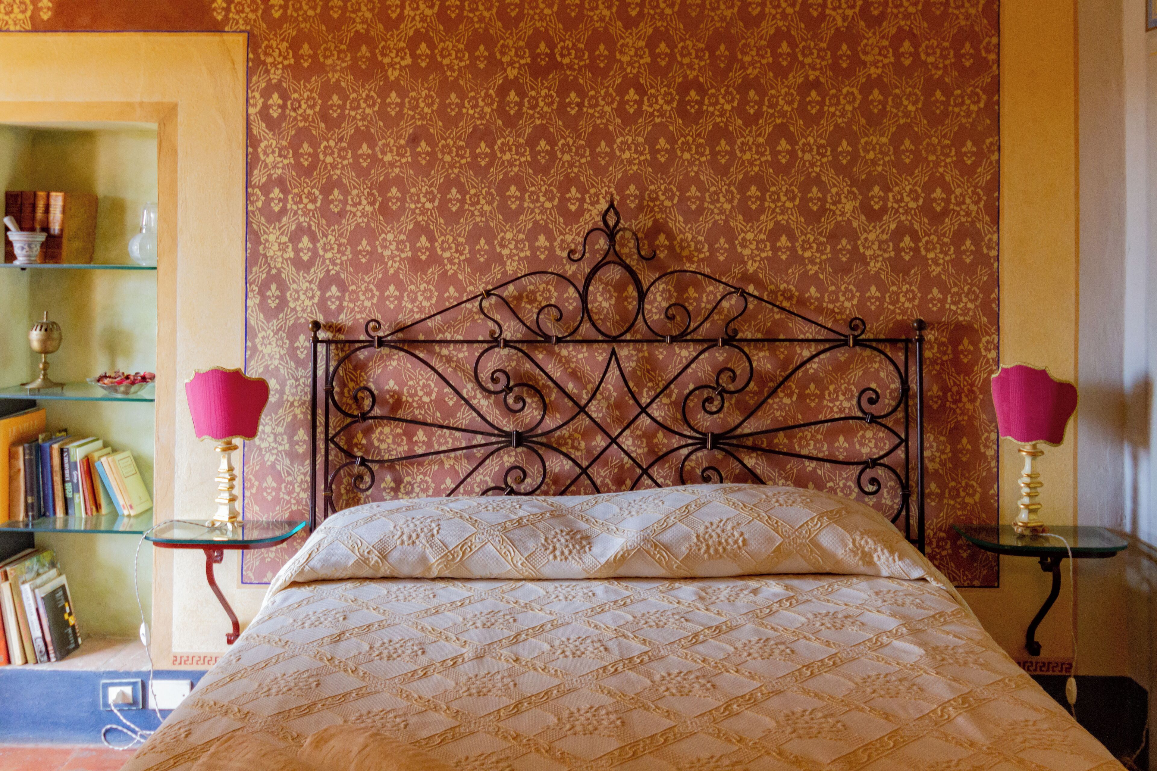 A neatly made bed with a patterned bedspread, a decorative metal headboard, and two bedside tables with lamps.