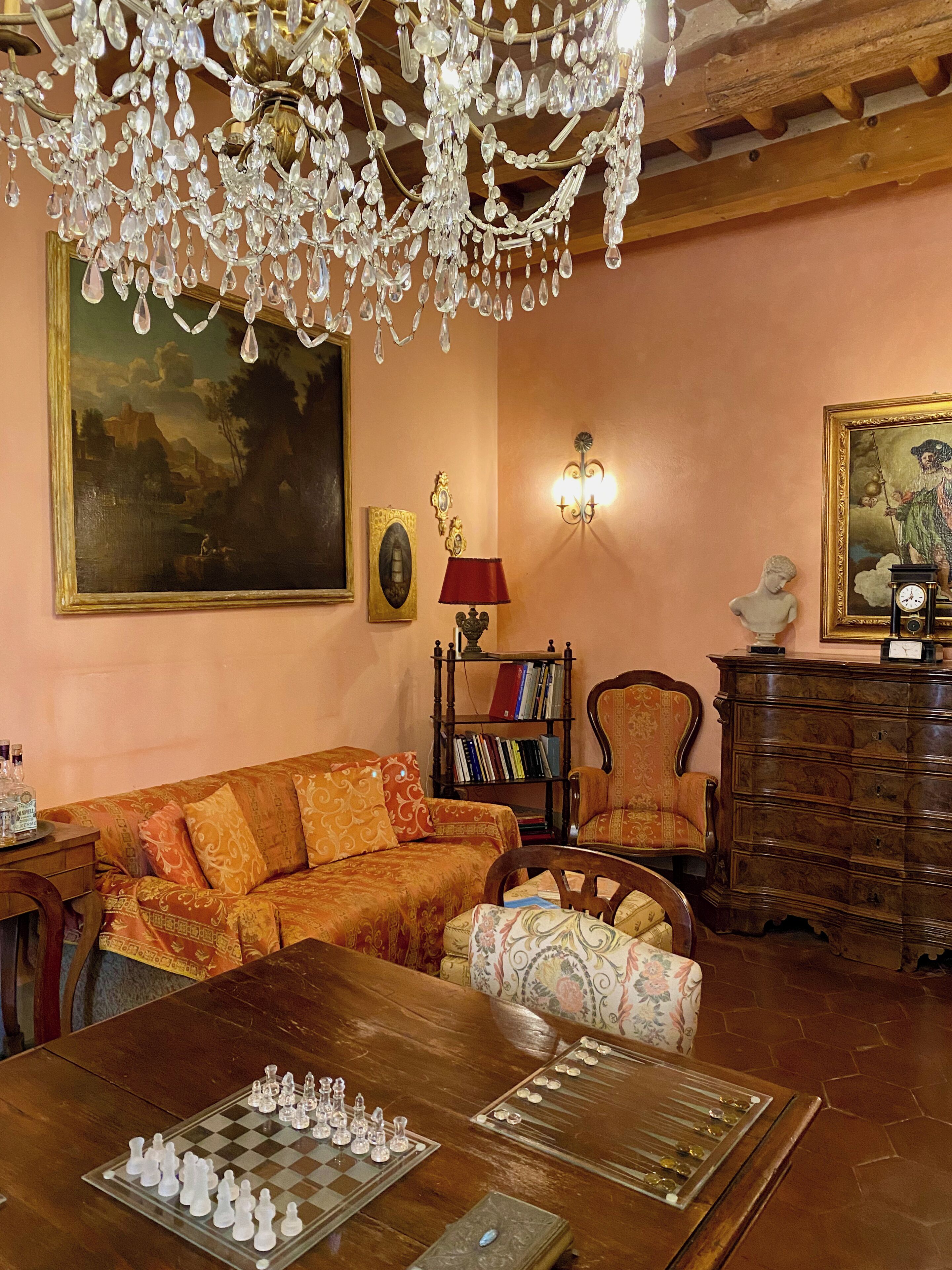 A cozy living room with a wooden coffee table, a sofa, a chair, a bookshelf, and a chandelier.
