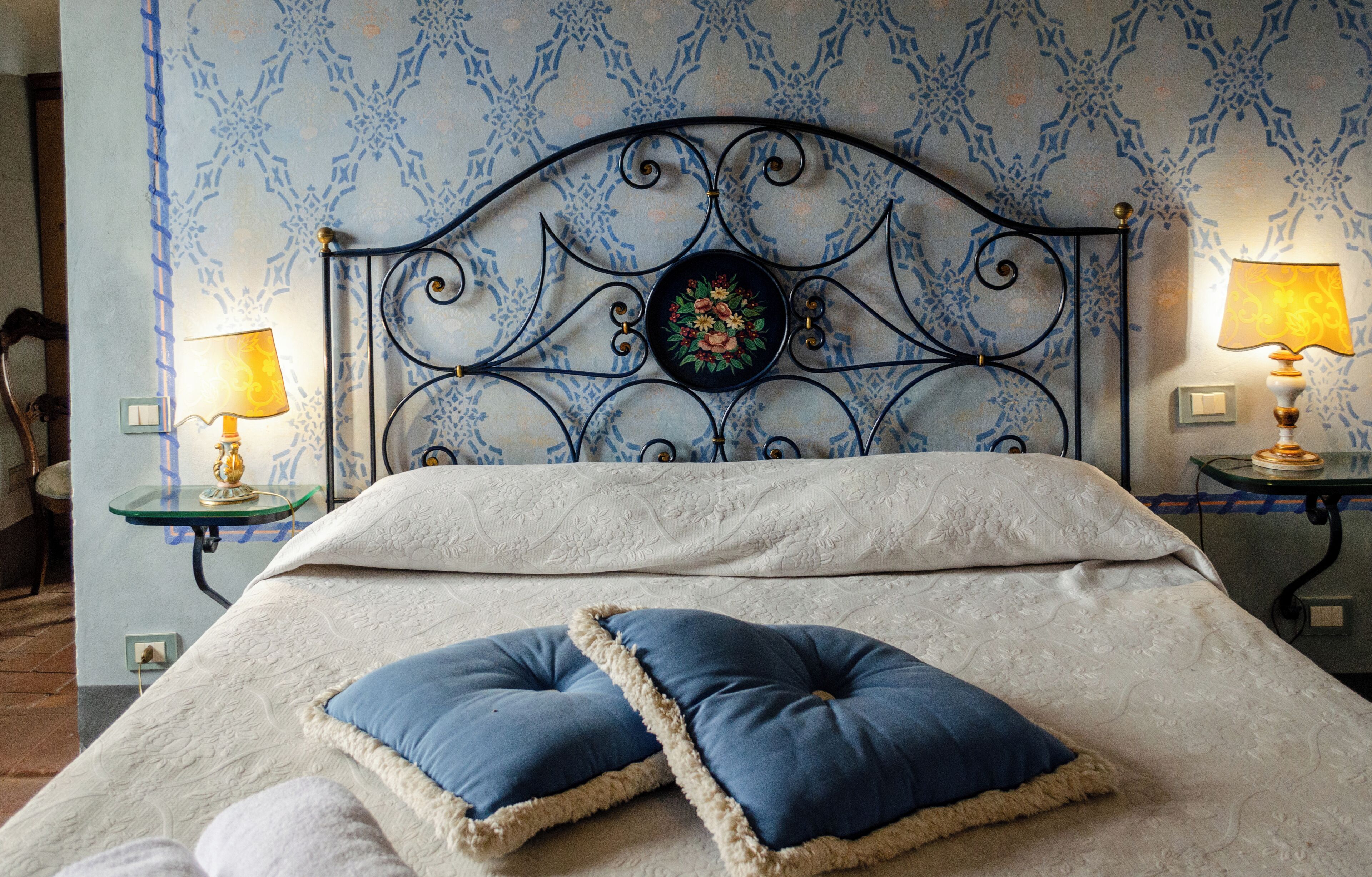 Una cama bien hecha con un cabecero decorativo, dos lámparas de noche y un estampado floral en la pared.