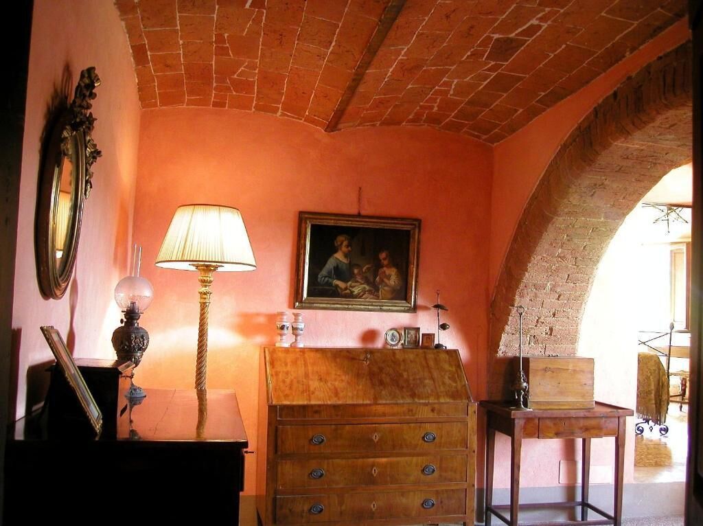 A room with a brick ceiling, a wooden dresser, a lamp, a framed painting, and a mirror.