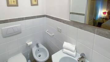 Une salle de bain comprenant des toilettes, un bidet et un lavabo, ainsi que deux reproductions botaniques encadrées accrochées au mur.