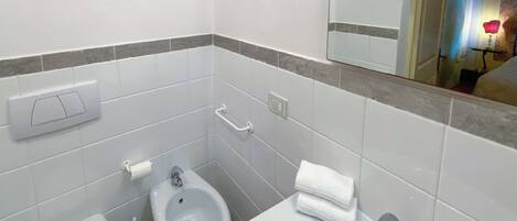 A bathroom with a toilet, bidet, and sink, along with two framed botanical prints on the wall.