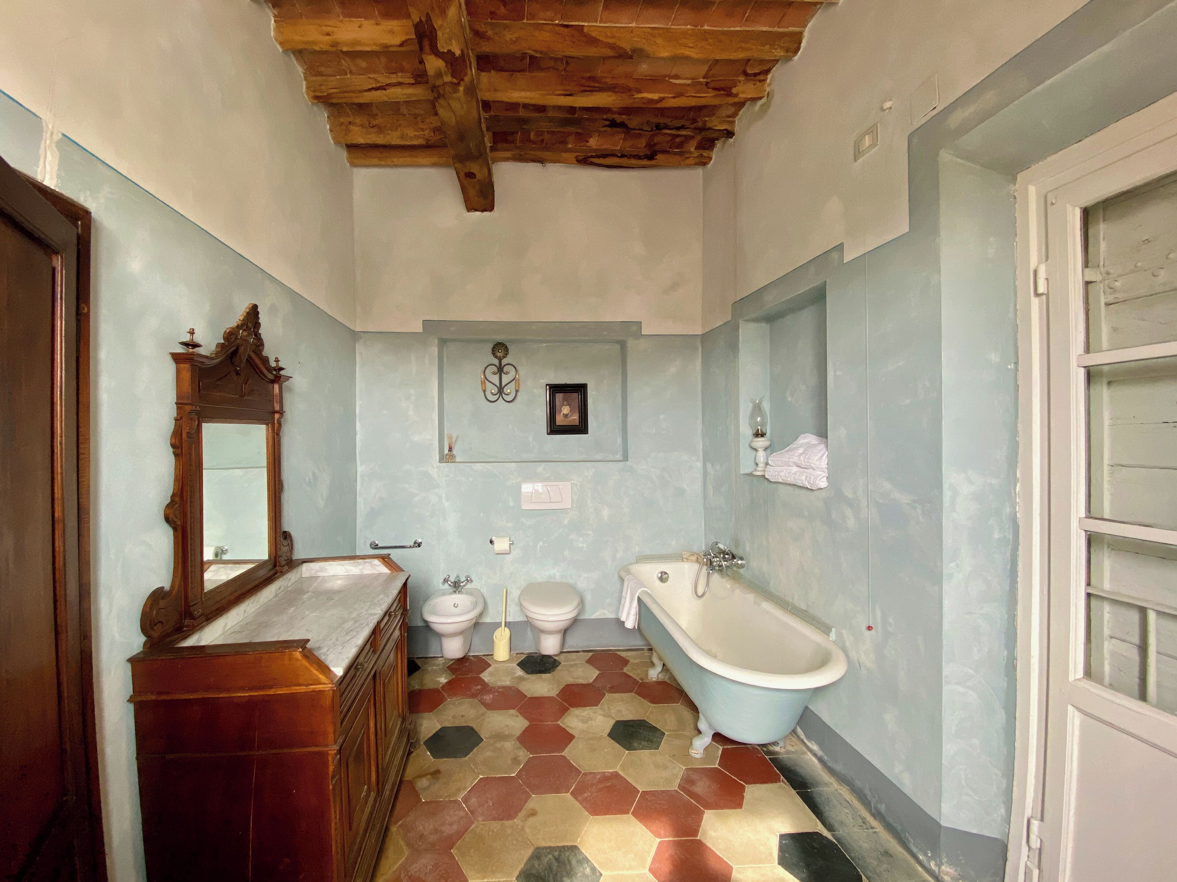 A bathroom with a wooden vanity, a clawfoot bathtub, and a hexagonal tiled floor.