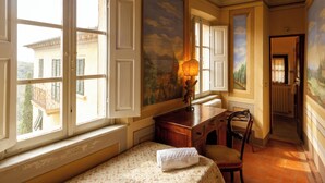 A room with a bed, a desk, a chair, and a window with open shutters.