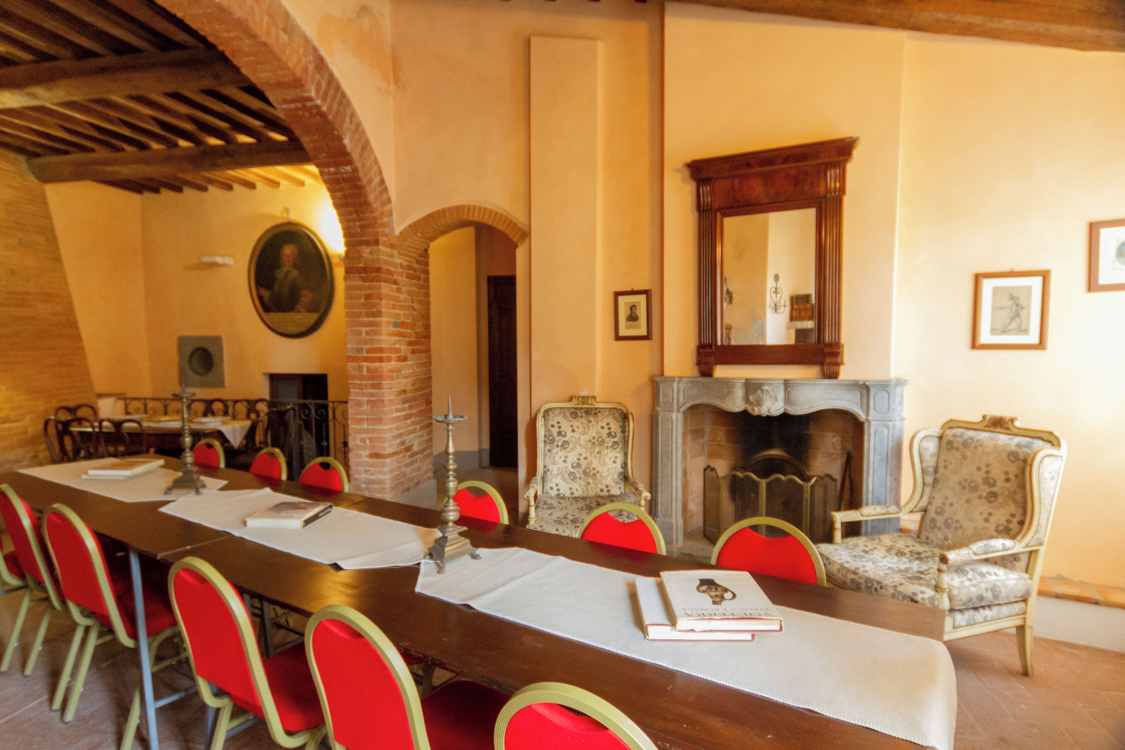A conference room with a long table, red chairs, a fireplace, and a mirror on the wall.