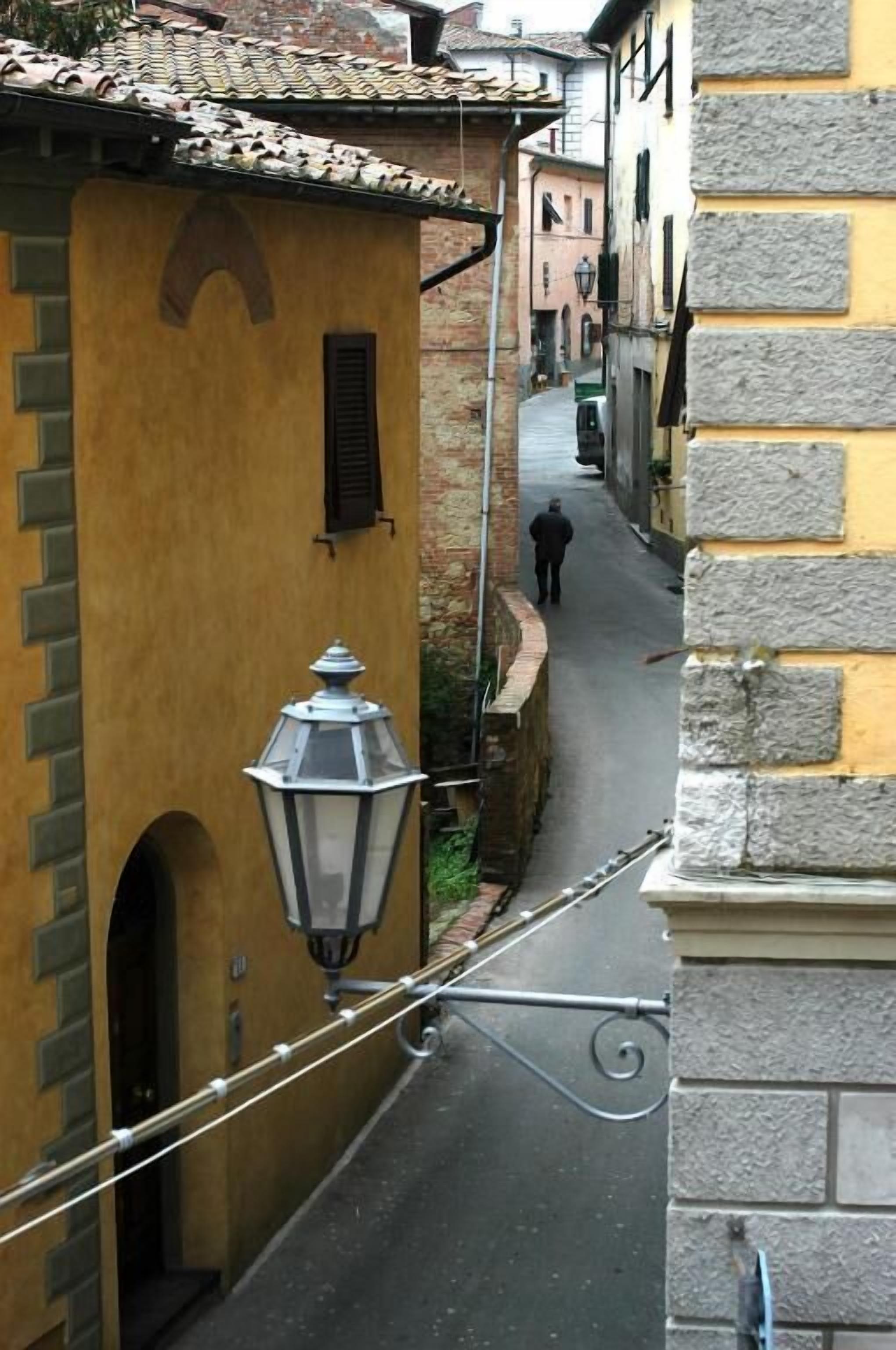 A narrow street with yellow and stone buildings, a person walking, and a street lamp.