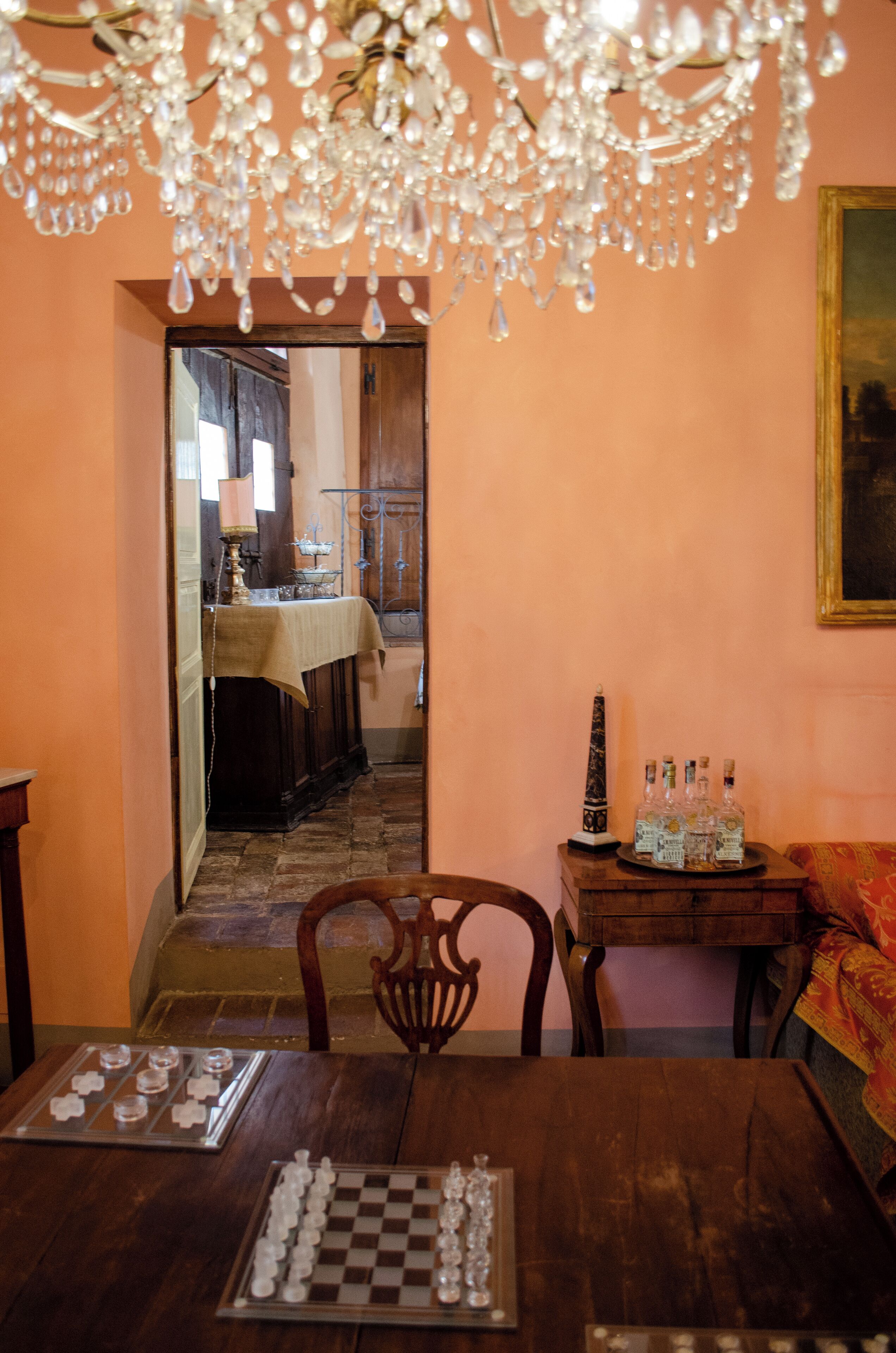 A wooden dining table with a chessboard, a chandelier, and a small table with bottles.