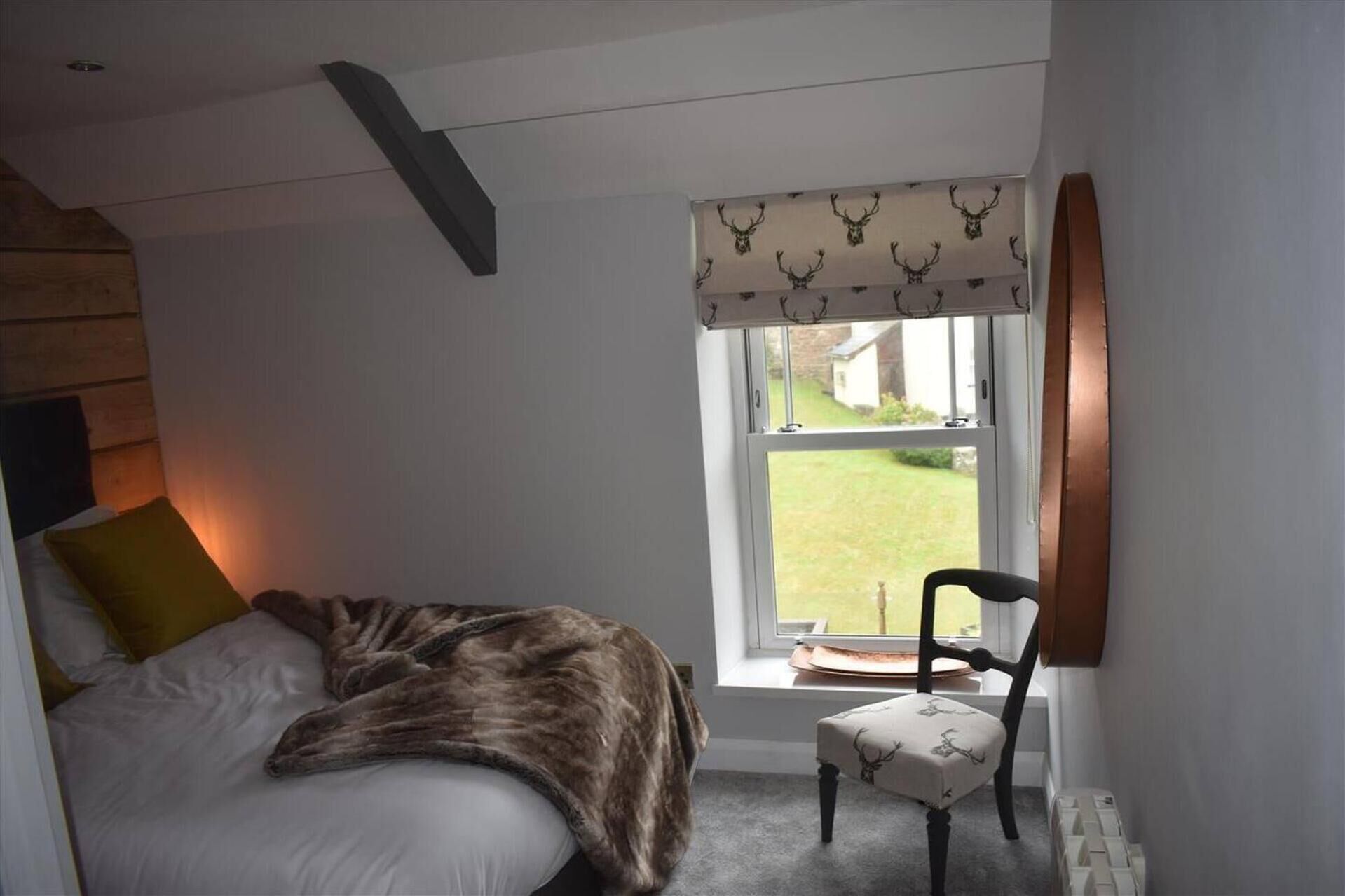 A bedroom with a bed, a chair, a window with a view of the outdoors, and a wooden sloped ceiling.