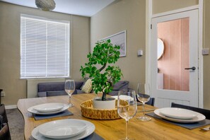 Un coin repas avec une table dressée pour deux personnes, une plante en pot et une porte dotée d’un panneau en bois.