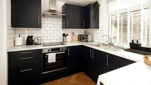 Una cocina moderna con gabinetes negros, azulejos blancos tipo metro, una campana extractora de acero inoxidable y un ventanal con persianas.
