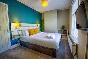 Une chambre d’hôtel avec un lit, une table de chevet, une lampe et une fenêtre avec des stores.